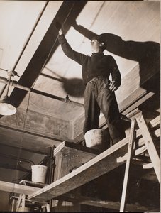 [En man som står på en träställning målar ett tak] av Arnold Eagle