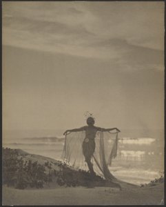 [Bakifrån av en dansare iförd en skir dräkt på stranden]