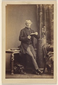 [Oidentifierad man sitter på ett bord och håller i en uppslagen bok] av Camille Silvy