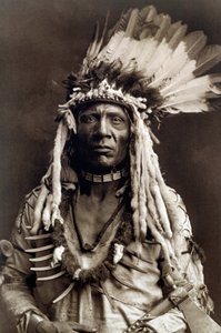 Vesselsvans (Apohsuyis). Porträtt av indianhövdingen för Piegan-stammen bär den berömda örnfjädern och vessla huvudbonaden, en mocka tunika, två halsband, ett i ben och det andra i grizzly klor, och en tomahawk pipa av Edward Sheriff Curtis