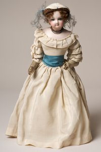 Bisque modedocka med vridbart huvud, klädd i en lång krämfärgad klänning och hatt (keramik och textil) av English School