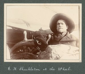E H Shackleton står vid hjulet på "Discovery" (1901) Från album av Sir Ernest Henry Shackleton med titeln National Antarctic Expedition (1901-1903) av Ernest Henry Shackleton