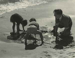 Tre barn leker med sand på stranden.