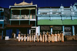 Buddhistiska nunnor i olika åldrar paraderar på trottoaren och ber om allmosor. Maymyo, Burma. av James L Stanfield