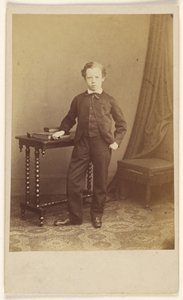 [Oidentifierad liten pojke i kostym står vid ett bord med böcker ovanpå] av Joseph Brown