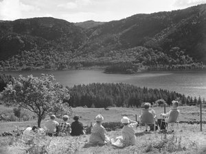 Grupp av människor som sitter på gräs eller solstolar och tittar på en utsikt över Thirlmere av Joseph Hardman