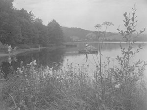 Man som fiskar i en båt på Estwaite Water och två flickor vid vattenbrynet