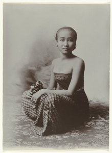 Studioporträtt av en sittande ung javanesisk kvinna i en sarong med batikmotiv