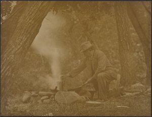 [Man som lagar mat över en lägereld i skogen] av Louis Fleckenstein