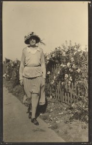 [Kvinna som går längs staket med blommor] av Louis Fleckenstein