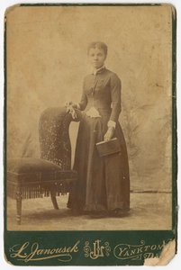 Fotografi av en kvinna som står bredvid en stol och håller i en bok, sent 1800-tal. av Louis Janousek
