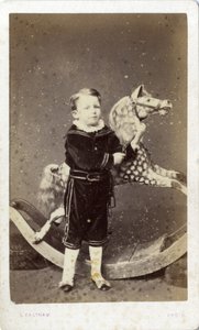 Ung pojke som står vid en gunghäst av Silas Eastham