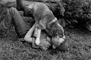 Ung man leker med sin hund utanför sin timmerstuga i Palmer, Alaska