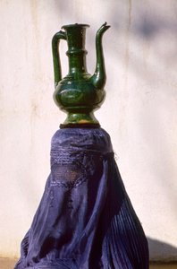 Kvinna i Kabul som är skyddad från insyn av en chadri aka chador-slöja i siden bär en kanna från en...