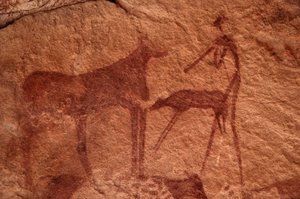Hällkonst, förhistorisk: Stenmålning av en ko, kalv och karaktär (bågskytt) i ett utsmyckat skydd, i Uweinat-massivet, Egypten. (Period från 8000 till 3000 år f.Kr.). Fotografi av Unbekannt