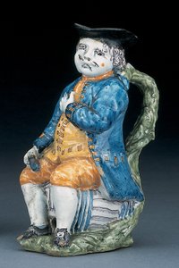 Tobykanna med ansikte och händer i blek mangan, hållande och tom klotformad buff-färgad kanna i tvättad blå jacka och byxor och grön väst, ca 1800 av Unbekannt