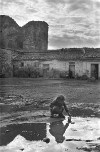 Ung flicka som leker med en pappersbåt i en pöl omgiven av lera, Venosa, Basilicata, Italien av Unbekannt