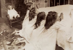 Fyra små flickor knäböjer vid sidan av en säng när de ber sin kvällsbön. av Unknown photographer
