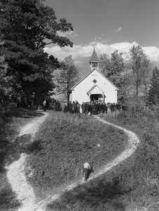 Män samlades utanför en liten byggnad på landsbygden, ett skolhus eller en kyrka med klocka...