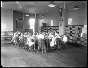 Barn lyssnar på en kvinna i läsrummet i en oidentifierad filial av Queens Borough Public Library, ca 1910 (s/v foto) av William Davis Hassler