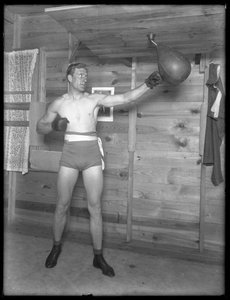 Engelske boxaren William Thomas Wells (Bombardier Billy Wells), poserar i träningsbyxor med en speedbag, ca 1911.
