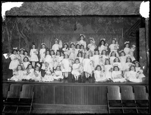Grupp av små flickor som poserar på en liten scen med dockor i handen, troligen från det romersk-katolska barnhemmet, Kingsbridge, Bronx, omkring 1911.