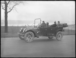 Tre oidentifierade personer och två Chow-hundar som kör i en cabriolet bil längs en flod eller sjö, ca 1912 av William Davis Hassler