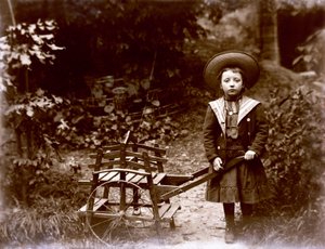 Flicka med vagn i en trädgård, tidigt 1900-tal (s/v foto) av . .