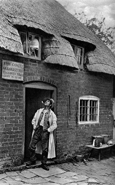 En man röker pipa utanför en butik, Worcestershire, c1922. av A. W. Cutler