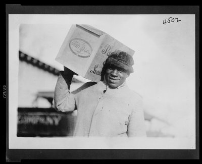 Afroamerikansk man bär ett fodral med "Four Roses"-whisky på axeln, möjligen konfiskerad av U.S. Internal Revenue Bureau av American Photographer