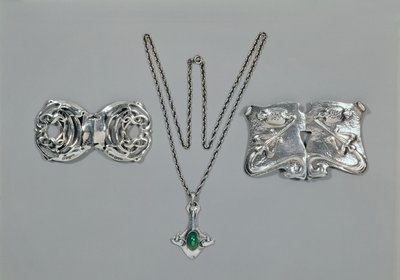 Silversmycken designade för Liberty. Vänster till höger: Midjelås med sammanflätad keltisk design, 1904. Hänge och kedja med cabochonskuren krysopras. Midjelås med repouse-design på hamrad av Archibald Knox