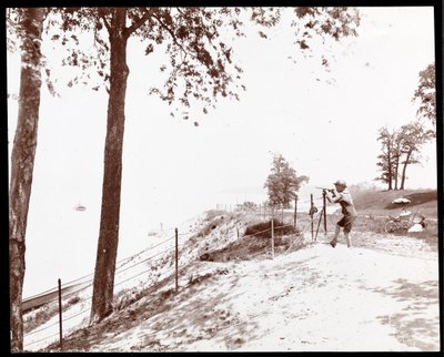 Vy över en pojke med ett kikare som tittar mot Hudsonfloden från Riverside Park, New York (silvergelatintryck) av Byron Company