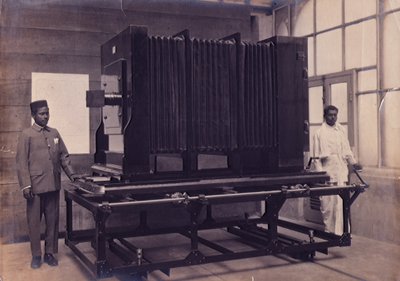 Två indiska assistenter som står bredvid den massiva kameran i den fotografiska avdelningen för Survey of India, ca 1911 (foto) av English Photographer