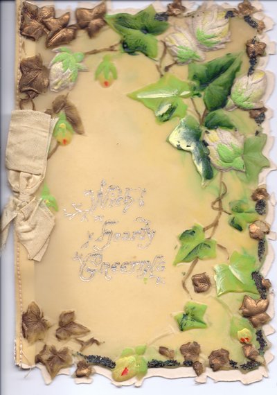 Ett gratulationskort av plast med guld och grön präglad murgröna och en beige rosett, cirka 1910 av English School