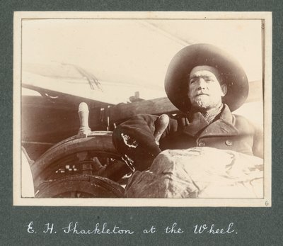E H Shackleton står vid hjulet på "Discovery" (1901) Från album av Sir Ernest Henry Shackleton med titeln National Antarctic Expedition (1901-1903) av Ernest Henry Shackleton