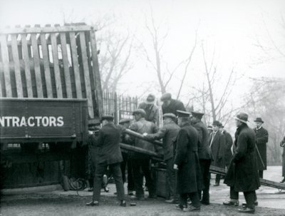 En skara åskådare står bredvid när en noshörning lastas av från en lastbil, av djurhållare, på London Zoo 1924 av Frederick William Bond