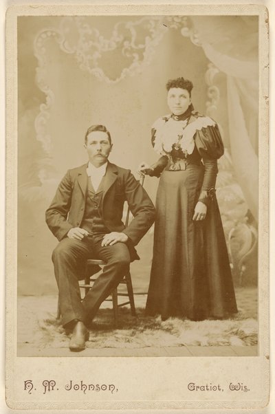 [Oidentifierat par: man med mustasch sittande, kvinna stående] av H. M. Johnson