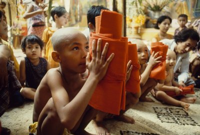 En ung pojke med rakat huvud får sin munkklädsel. Mandalay, Burma. av James L Stanfield