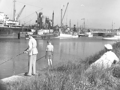En man och en pojke fiskar i Glasson Dock medan en kvinna är till sjöss; havslandskap; bakom ser Ted på, olika båtar förtöjda av Joseph Hardman