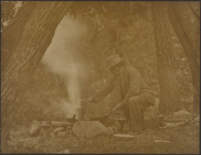 [Man som lagar mat över en lägereld i skogen] av Louis Fleckenstein