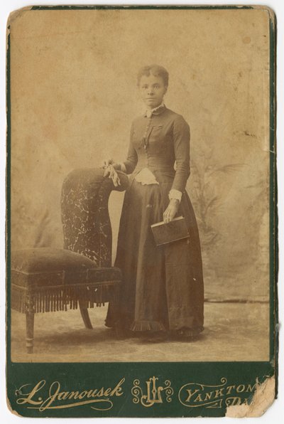 Fotografi av en kvinna som står bredvid en stol och håller i en bok, sent 1800-tal. av Louis Janousek