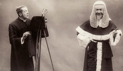 En man i en socka riktar linsen på sin kamera mot en man klädd som en påve av Rotary Photographic Co Ltd