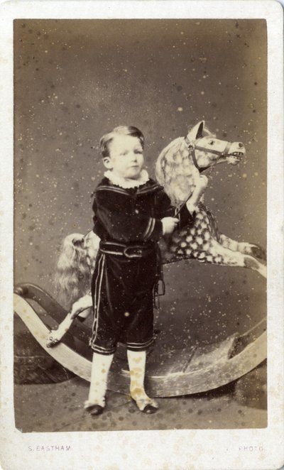 Ung pojke som står vid en gunghäst av Silas Eastham