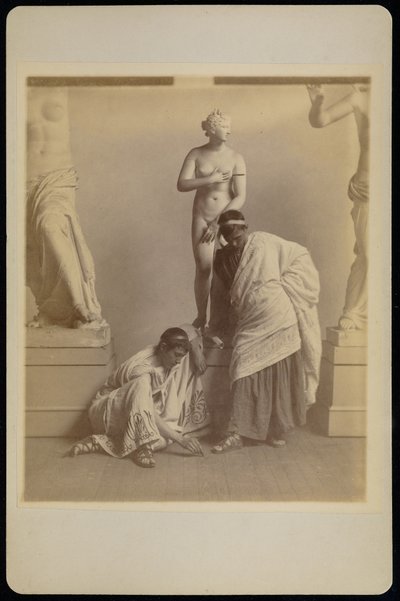 [Två manliga studenter i grekisk dräkt framför en gipsavgjutning av Afrodite i avgjutningsrummet på Pennsylvania Academy]. av Thomas Eakins