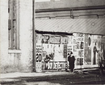 En man går förbi en vägg med affischannonser, inklusive en för Johnnie Hoey The Boy Detective som spelar på Havlins teater på 600 Walnut Street. av Unbekannt