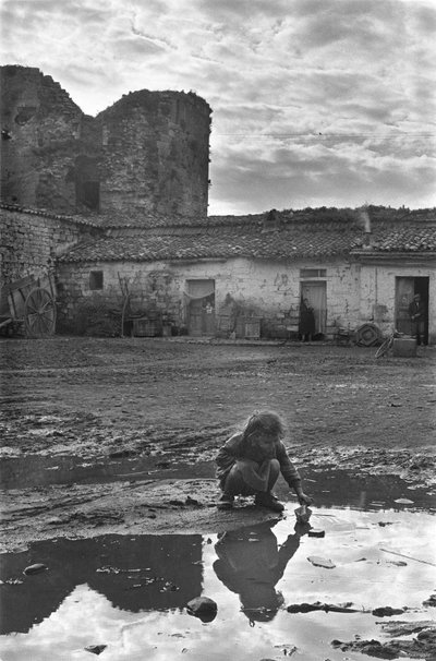 Ung flicka som leker med en pappersbåt i en pöl omgiven av lera, Venosa, Basilicata, Italien av Unbekannt