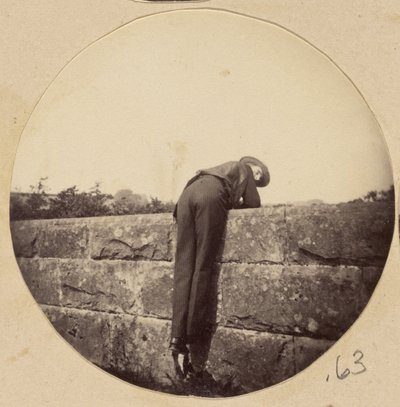 [Man i hatt böjd över en stenmur] av Unknown artist