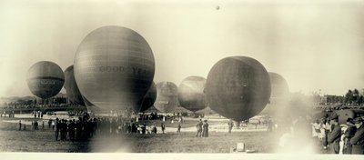 Hot air balloons at a field in South St. Louis ready for launch; one is already in the sky in the distance av W.C. Persons