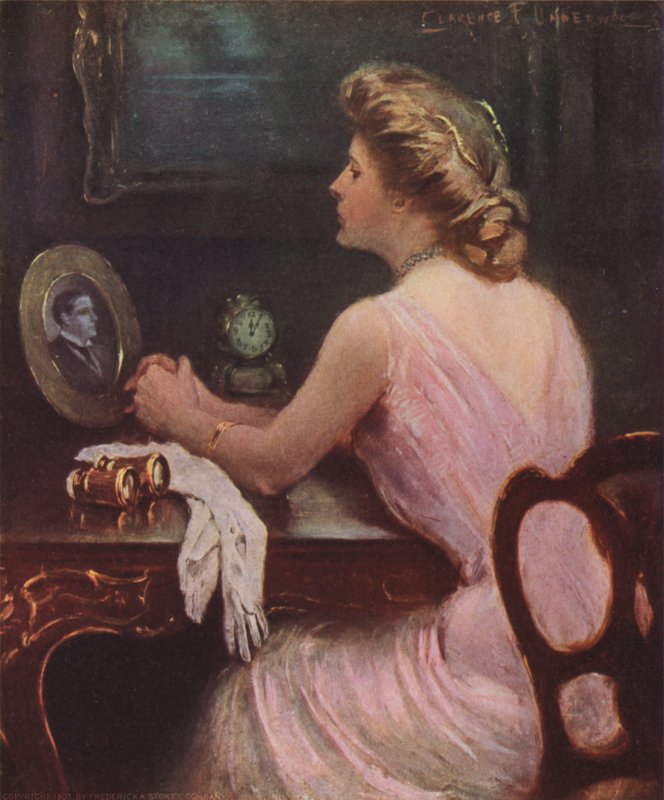 Kvinna som sitter vid sitt sminkbord och tittar på ett fotografi av en man, möjligen hennes man eller älskare av Clarence F. Underwood