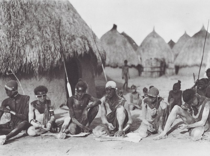 Afrika: Shilluk-krigare gnider in sig med träaska (svartvitt foto) av Hugo Adolf Bernatzik